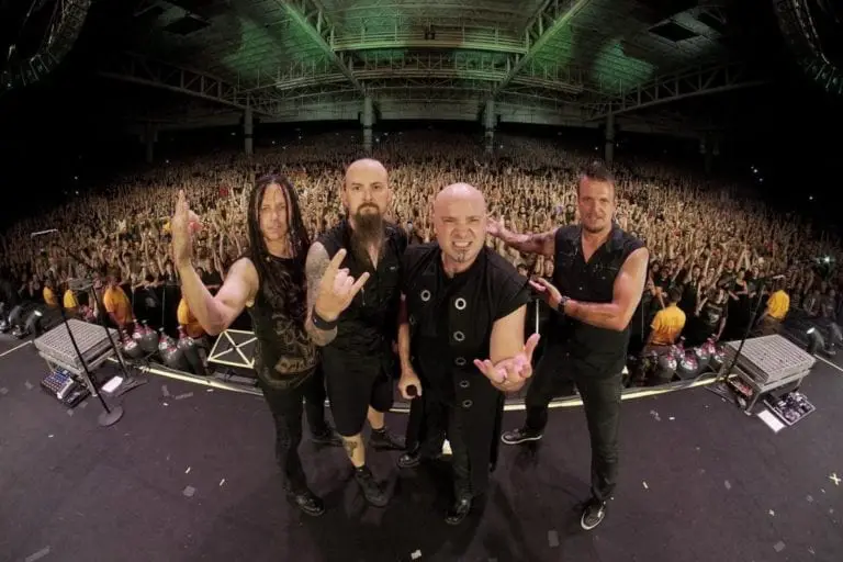 Members of the band Disturbed pose on stage as the crowd behind them cheers.