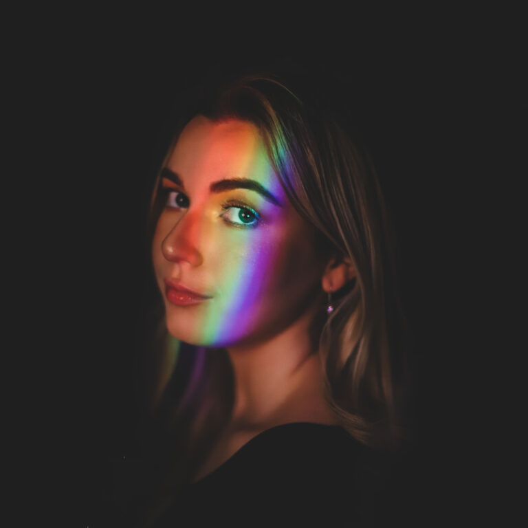 Sabrina Trueheart in a dark room with her face illuminated by rainbow light.