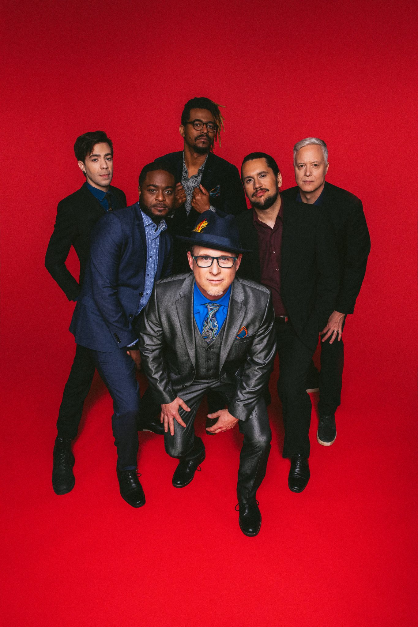 Nation Beat, a jazz group of six, poses in front of a red background, with drummer Scott Kettner standing in front.