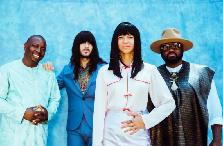 Khruangbin trio pose in front of blue wall with Vieux Farka Touré