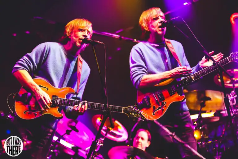 Phish singer Trey Anastasio plays the guitar and sings into a microphone during a live performance. 