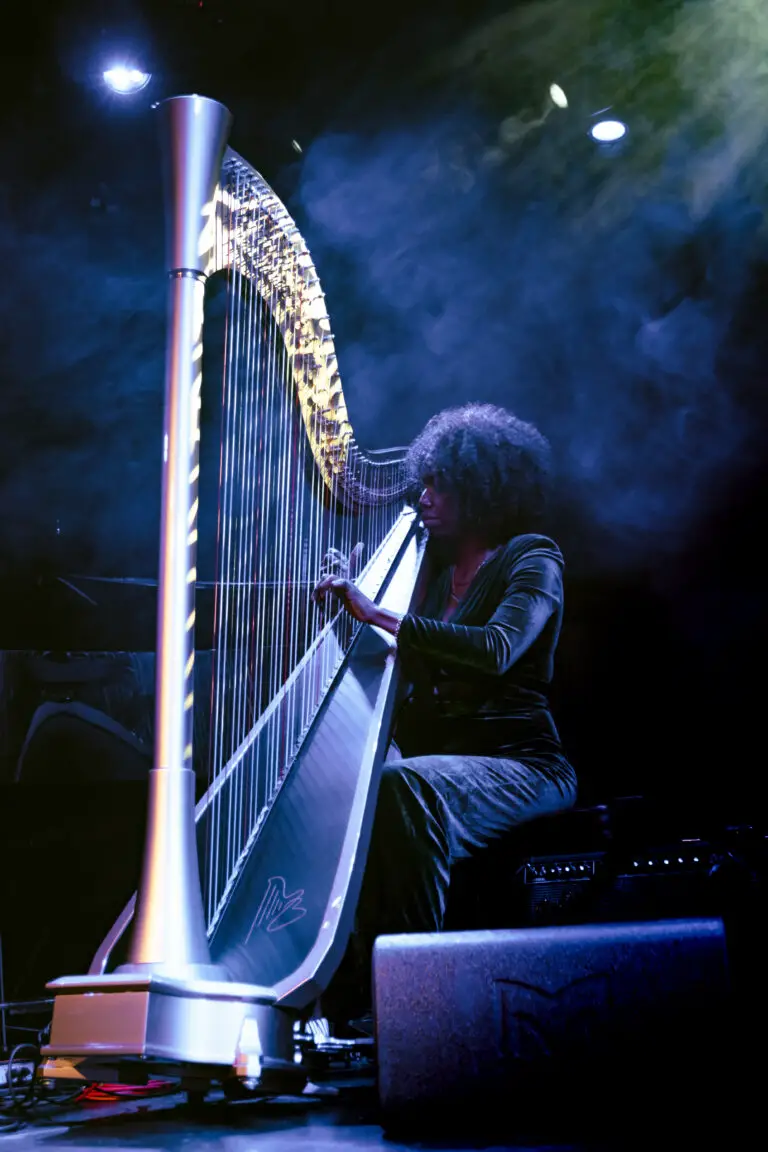 Brandee Younger playing the harp with blue smoke and golden light illuminating her.
