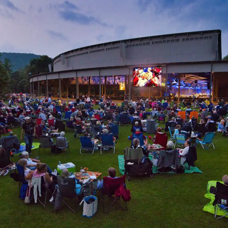 Tanglewood photo from back of the lawn as the sun has set with an orchestra playing on stage and people on lawn chairs in the lawn area