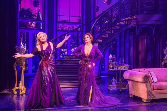 picture from Death Becomes Us performance. Lead actresses in purple on purple and blue living room set stage.