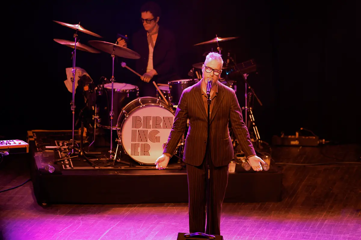 Matt Berninger, the lead singer of The National, performs a solo set at Webster Hall in New York City. He is pictured with his eyes closed singing into the microphone in front of Sterling Laws on the drumkit.